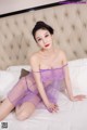 A woman in a purple lingerie sitting on a bed.