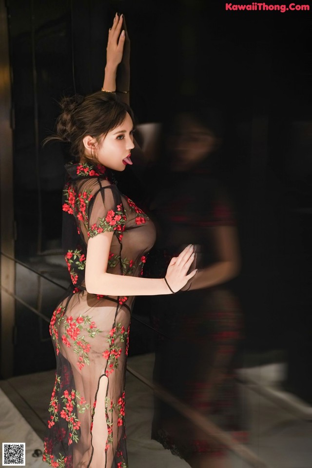 A woman in a sheer black dress with red flowers on it.