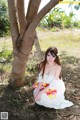 A woman in a white dress sitting under a tree.