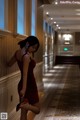 A woman in a red dress leaning against a wall.