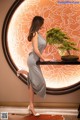 A woman in a gray dress standing next to a table with a bonsai tree.