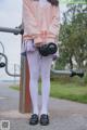 A woman in a pink cardigan and white tights holding a pair of dumbbells.