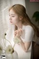 A woman sitting at a window sill with a vase of flowers.