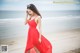 A woman in a red dress standing on a beach.