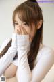 A woman in a white shirt covering her face with her hands.