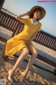 A woman in a yellow dress and hat sitting on a bench.